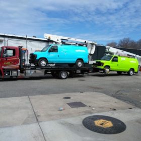 A tow truck towing two trucks on the back of a trailer.